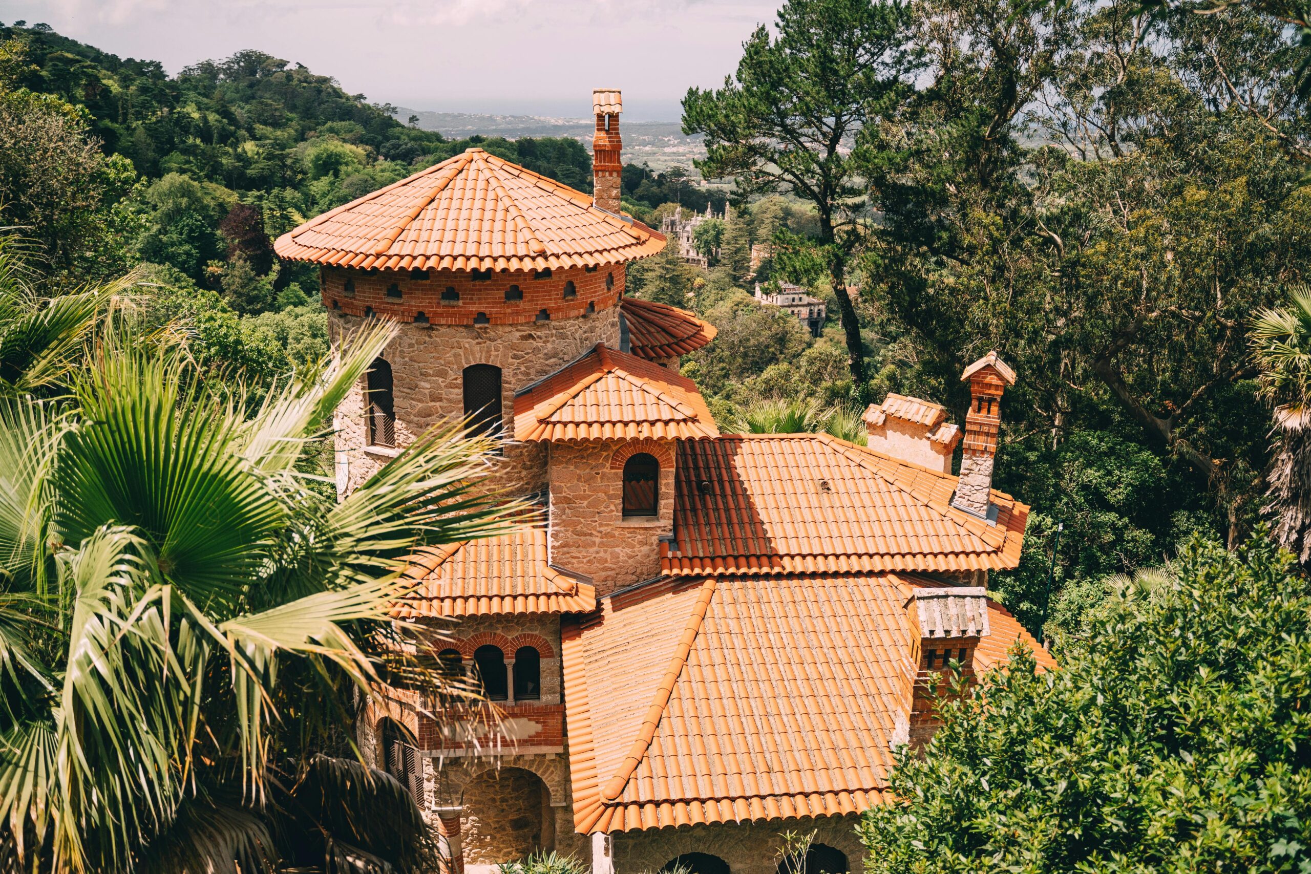 Elevated view of Vila Sassetti in lush Sintra, showcasing red-tiled roofs and surrounding greenery.